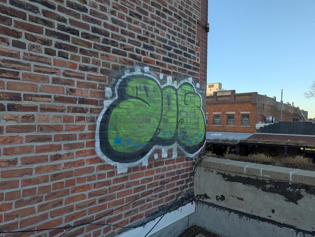 Before: green and black graffiti spray-painted on a brick wall on an Old Market rooftop.